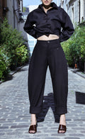 Pantalon Dune Noire en gabardine de laine japonaise, coupe barrel, porté de face dans une rue pavée