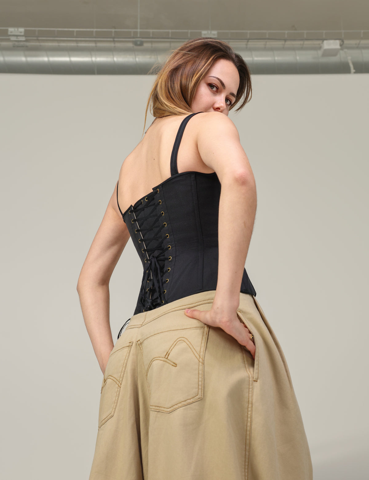 Corset Eve noir en ottoman de soie porté de dos, avec le pantalon Dune en coton sable