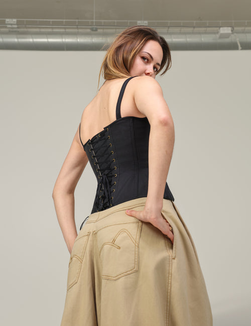 Corset Eve noir en ottoman de soie porté de dos, avec le pantalon Dune en coton sable